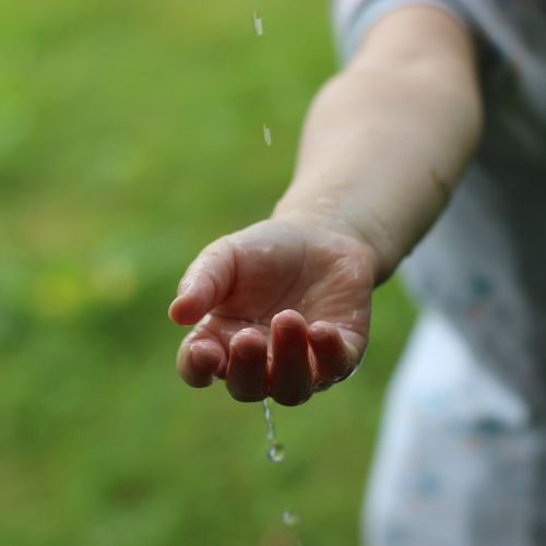 Kinderhand mit fallenden Wassertropfen